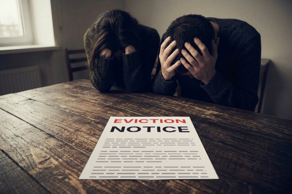 A couple sit with their heads in their hands at a table, an eviction notice in front of them